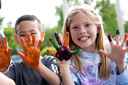Un niño y una niña mostrando las manos cubiertas de pintura